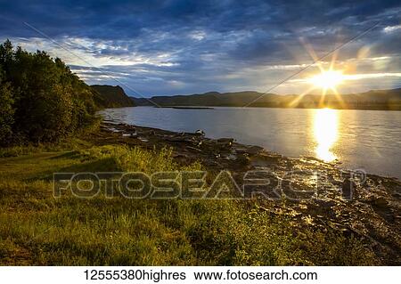 Stock Photograph - Sun going down on the Yukon River in summer; Alaska, United States of America. Fotosearch