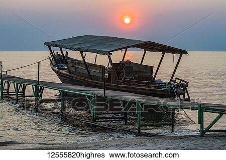 Stock Photograph - Sun setting behind boat moored to dock at Mbali Mbali Mahale Lodge (Kungue Beach Lodge) on Lake Tanganyika; Tanzania. Fotosearch