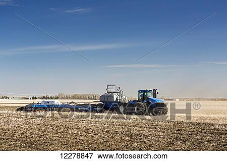 Stock Photo - Tractor and air seeder with nitrogen tank in stubble field planting crop with blue sky and clouds; Alberta, Canada. Fotosearch