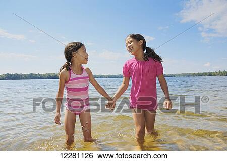 Stock Photograph - Two sisters holding hands and playing in Crystal lake; Ontario, Canada. Fotosearch