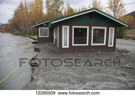 Stock Photo - View of a house in danger of collapsing into the flooding Matanuska River, Palmer, Southcentral Alaska, autumn. Fotosearch