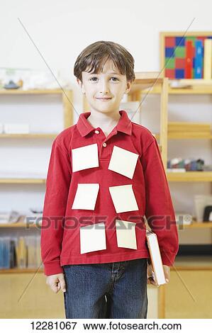 Stock Photo - Young boy standing in classroom with sticky notes on shirt; Toronto, Ontario, Canada. Fotosearch