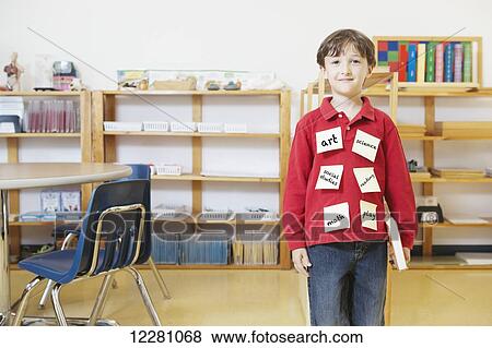 Stock Photo - Young boy standing in classroom with sticky notes on shirt; Toronto, Ontario, Canada. Fotosearch