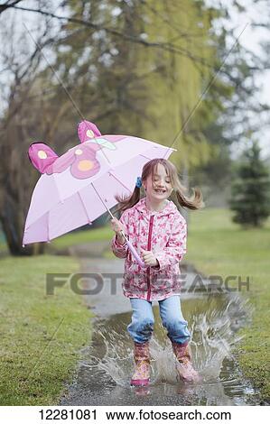 Stock Image - Young girl jumping in puddle while holding umbrella; Toronto, Ontario, Canada. Fotosearch