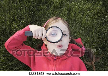 Young girl laying in grass holding a magnifying glass; Toronto, Ontario, Canada View Large Photo Image Stock Image - Young girl laying in grass holding a magnifying glass; Toronto, Ontario, Canada. Fotosearch