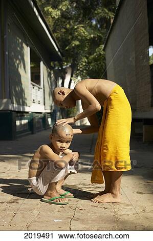 Stock Image - Young Monk Shaving Another's Head, Mandalay, Myanmar (Burma). Fotosearch