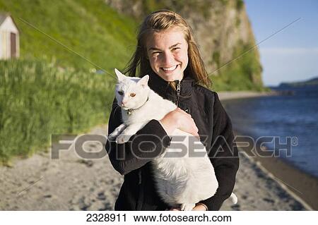 Stock Image - A Girl Holding Her White Cat On The Beach At Her Family's Fish Camp; False Pass, Alaska, United States Of America. Fotosearch