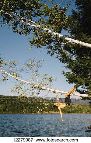 A young man hanging on to a tree branch leaning out over a lake; Waterbury, Vermont, United States of America View Large Photo Image Stock Photo - A young man hanging on to a tree branch leaning out over a lake; Waterbury, Vermont, United States of America. Fotosearch