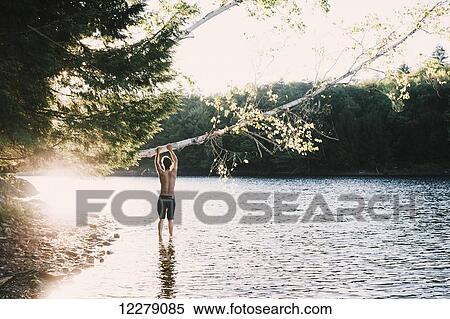 A young man stands at the edge of a lake holding on to a leaning tree; Waterbury, Vermont, United States of America View Large Photo Image Stock Photography - A young man stands at the edge of a lake holding on to a leaning tree; Waterbury, Vermont, United States of America. Fotosearch