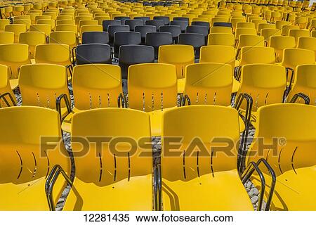 Stock Photography - Black chairs amongst rows of yellow plastic chairs in rows; Locarno, Ticino, Switzerland. Fotosearch