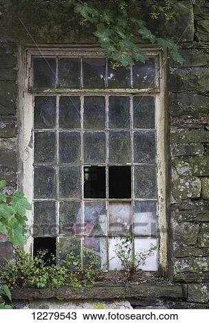 Stock Image - Broken panes of glass missing in a window of a stone building; Cumbria, England. Fotosearch