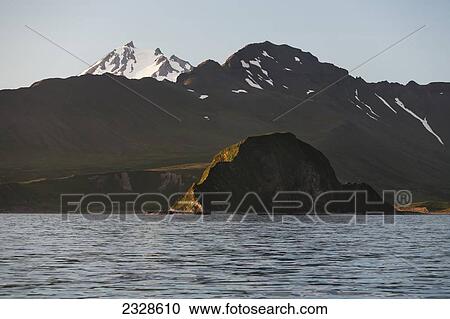 Frosty Volcano Peaking Out From Behind A Ridgeline With Aagat Island In The Foreground Near Cold Bay On The Alaska Peninsula; Southwest Alaska, United States Of America View Large Photo Image Stock Image - Frosty Volcano Peaking Out From Behind A Ridgeline With Aagat Island In The Foreground Near Cold Bay On The Alaska Peninsula; Southwest Alaska, United States Of America. Fotosearch