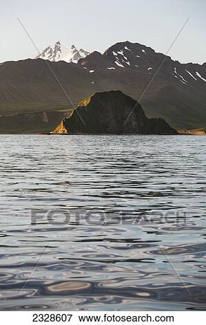 Stock Photo - Frosty Volcano Peaking Out From Behind A Ridgeline With Aagat Island In The Foreground Near Cold Bay On The Alaska Peninsula; Southwest Alaska, United States Of America. Fotosearch