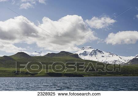 Stock Photography - Green Shores And Snow Covered Roundtop Mountain On Unimak Island, The Easternmost Island Of The Aleutian Chain, From Ikatan Bay; Southwest Alaska, United States Of America. Fotosearch
