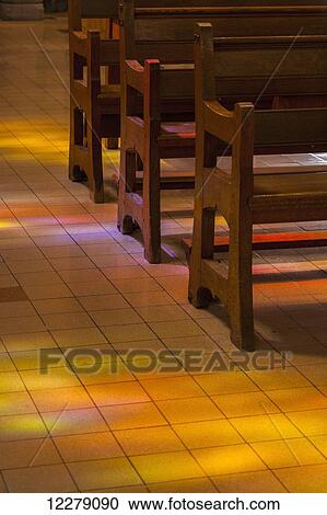 Stock Image - Light from stained glass windows shining on floor and wooden pews, St. Michael's Cathedral and Basilica, circa 1959; Sherbrooke, Quebec, Canada. Fotosearch