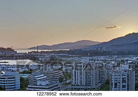 Stock Image - Looking west towards West Vancouver, Bowen Island and the Lions Gate Bridge in the late afternoon sun at North Vancouver; Vancouver, British Columbia, Canada. Fotosearch