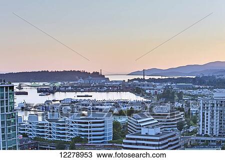 Stock Image - Looking west towards West Vancouver, Bowen Island and the Lions Gate Bridge in the late afternoon sun at North Vancouver; Vancouver, British Columbia, Canada. Fotosearch