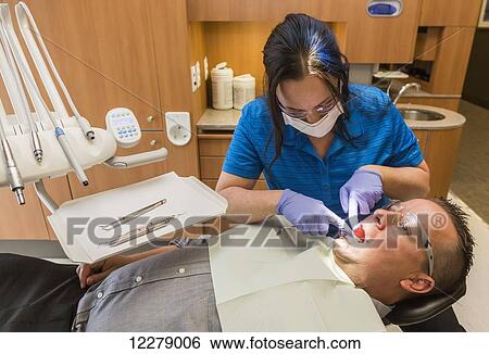 Male patient in dental chair during a dental procedure performed by a dental assistant; Edmonton, Alberta, Canada View Large Photo Image Stock Photograph - Male patient in dental chair during a dental procedure performed by a dental assistant; Edmonton, Alberta, Canada. Fotosearch