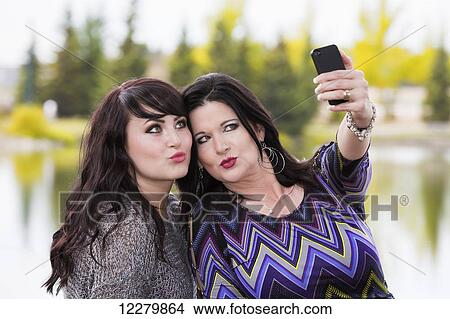 Picture - Mother and daughter spending quality time together and taking a selfie outdoors in a city park in autumn; St. Albert, Alberta, Canada. Fotosearch