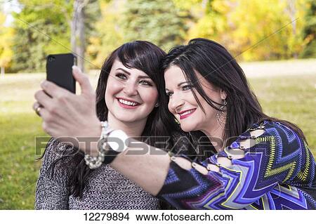Picture - Mother and daughter taking a selfie in a city park in autumn; St. Albert, Alberta, Canada. Fotosearch