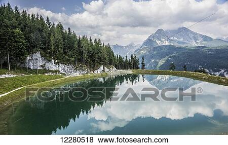 Stock Photo - Mountain and forest reflected in a lake and a hiking trail around the lake; Berchtesgadener Land, Bavaria, Germany. Fotosearch