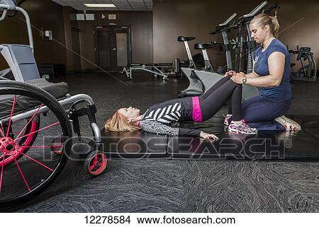 Picture - Physiotherapist assisting young woman with spinal cord injury in performing bridges exercises; Edmonton, Alberta, Canada. Fotosearch