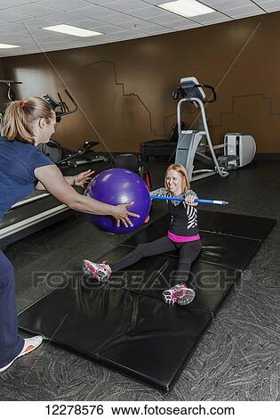 Physiotherapist assisting young woman with spinal cord injury in performing resistance ball toss exercises; Edmonton, Alberta, Canada View Large Photo Image Stock Photograph - Physiotherapist assisting young woman with spinal cord injury in performing resistance ball toss exercises; Edmonton, Alberta, Canada. Fotosearch