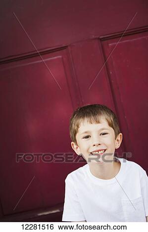 Stock Photograph - Portrait of a young boy in front of a red door; Nashville, Tennessee, United States of America. Fotosearch