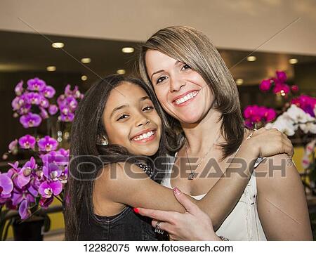 Stock Photography - Portrait of a young mother and her daughter posing in a mall in front of flowers; St. Albert, Alberta, Canada. Fotosearch