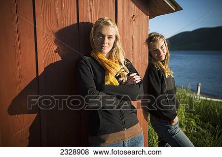 Stock Photo - Portrait Of Two Sisters Enjoying The Sunshine At Their Family's Fish Camp; False Pass, Alaska, United States Of America. Fotosearch