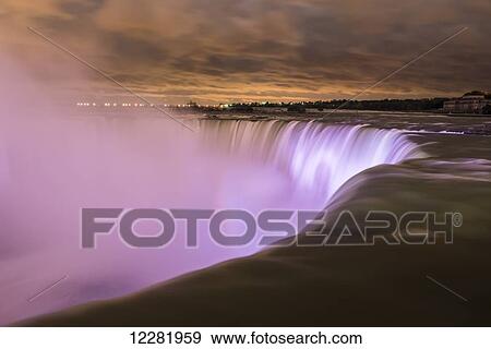 Stock Photo - Rays of light and magic colours of illuminated water of Niagara Falls at night; Niagara Falls, Ontario, Canada. Fotosearch