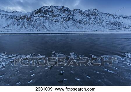 Snow Covered Landscape Along The Eastern Shore Of Iceland As A Stream Flows Gently Past With Ice Forming Along The Shore Of It; Iceland View Large Photo Image Stock Photo - Snow Covered Landscape Along The Eastern Shore Of Iceland As A Stream Flows Gently Past With Ice Forming Along The Shore Of It; Iceland. Fotosearch