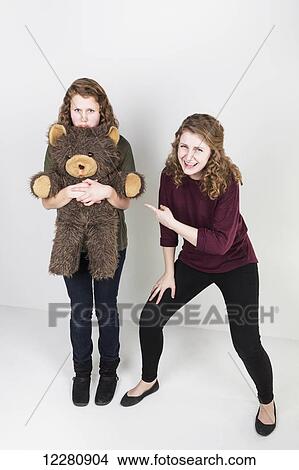 Studio shot of one friend making fun of another friend holding her teddy bear; Alberta, Canada View Large Photo Image Picture - Studio shot of one friend making fun of another friend holding her teddy bear; Alberta, Canada. Fotosearch