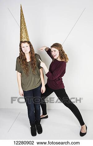 Studio shot of one friend making fun of another friend wearing a dunce cap; Alberta, Canada View Large Photo Image Stock Image - Studio shot of one friend making fun of another friend wearing a dunce cap; Alberta, Canada. Fotosearch
