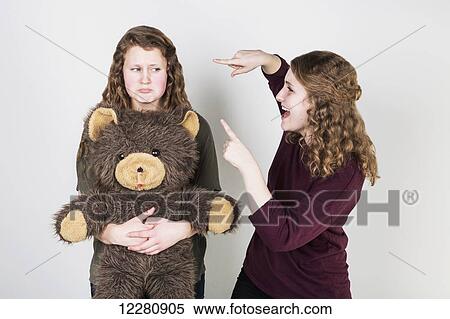 Studio shot of one friend making fun of another friend holding her teddy bear; Alberta, Canada View Large Photo Image Stock Photography - Studio shot of one friend making fun of another friend holding her teddy bear; Alberta, Canada. Fotosearch