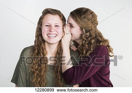 Stock Photo - Studio shot of one friend telling a secret to another friend, on a white background; Alberta, Canada. Fotosearch