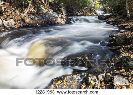 Stock Image - Sunlight and shadows are playing together on stony rapids near Emsdale town; Ontario, Canada. Fotosearch