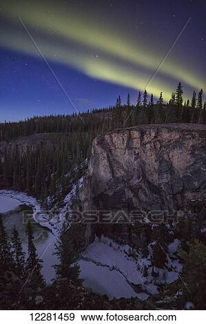 Stock Photo - The northern lights (aurora borealis) dance in the skies above Lapie River canyon; Whitehorse, Yukon, Canada. Fotosearch