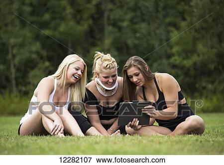 Stock Photo - Three teenage gymnasts looking at pictures on mobile device after practicing their routines in a park; Edmonton, Alberta, Canada. Fotosearch