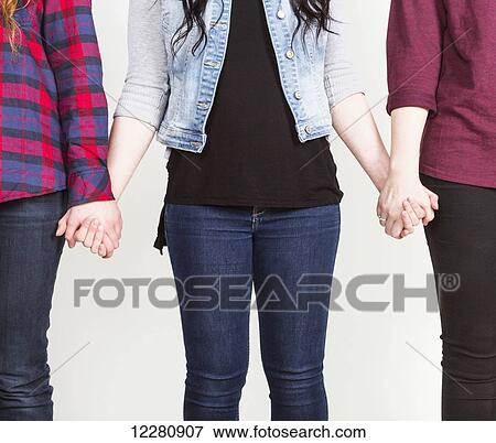 Three young women holding hands committed to teamwork; Alberta, Canada View Large Photo Image Stock Photo - Three young women holding hands committed to teamwork; Alberta, Canada. Fotosearch
