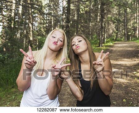 Stock Photo - Two girlfriends doing a selfie expression on a pathway in a park; Edmonton, Alberta, Canada. Fotosearch