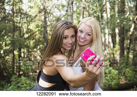 Stock Image - Two girlfriends posing for a selfie together in a park; Edmonton, Alberta, Canada. Fotosearch
