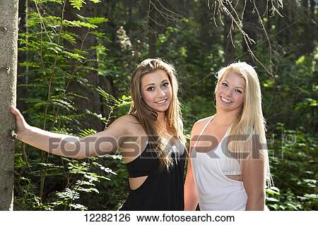Stock Photograph - Two girlfriends posing together in the woods in the sunshine; Edmonton, Alberta, Canada. Fotosearch
