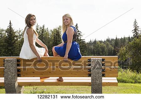 Two girlfriends sitting on a park bench in their dresses posing for a picture; Edmonton, Alberta, Canada View Large Photo Image Stock Image - Two girlfriends sitting on a park bench in their dresses posing for a picture; Edmonton, Alberta, Canada. Fotosearch