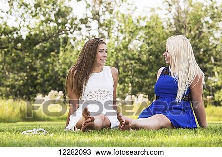 Stock Image - Two girlfriends spending time together in a park wearing dresses; Edmonton, Alberta, Canada. Fotosearch