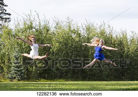 Two gymnast girlfriends practicing their split jumps in a park in their dresses; Edmonton, Alberta, Canada View Large Photo Image Stock Photograph - Two gymnast girlfriends practicing their split jumps in a park in their dresses; Edmonton, Alberta, Canada. Fotosearch