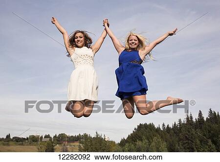 Two teenage athletes in dresses jumping high in the air in a park; Edmonton, Alberta, Canada View Large Photo Image Stock Image - Two teenage athletes in dresses jumping high in the air in a park; Edmonton, Alberta, Canada. Fotosearch