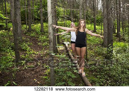 Stock Photo - Two teenage girlfriends balancing on a fallen log in the forest in a park; Edmonton, Alberta, Canada. Fotosearch