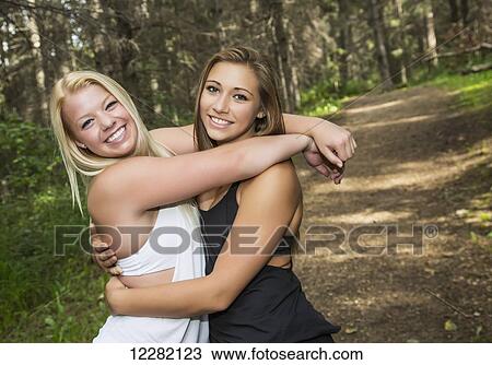 Stock Image - Two teenage girlfriends hugging on a path in a park and posing for a picture; Edmonton, Alberta, Canada. Fotosearch