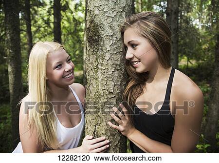 Two teenage girlfriends smiling at each other while hugging a tree together in a park; Edmonton, Alberta, Canada View Large Photo Image Stock Image - Two teenage girlfriends smiling at each other while hugging a tree together in a park; Edmonton, Alberta, Canada. Fotosearch